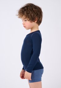 Maglietta a maniche lunghe blu navy con collo rotondo, abbinata a pantaloni corti azzurri chiari. Tessuto morbido, design aderente, cuciture minime e texture liscia.