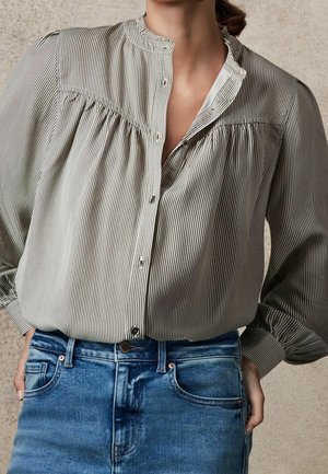 Kvinde iført en striped, knappet bluse med samlet skulderparti, stukket ned i blå denim jeans.