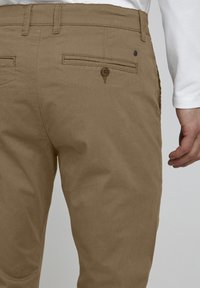 Kjempe bukser i khaki bomull med flat foran, sidelommer og en baklomme med knappelukking. Glatt tekstur og slim fit design.