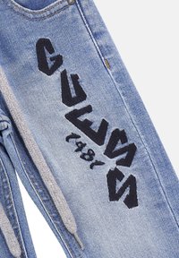 Joggers de mezclilla azul con un cordón gris y un bold bordado negro que presenta letras y un detalle del año. Textura suave, diseño casual.