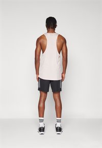 Ροζ αμάνικο μπλουζάκι με ανοιχτή πλάτη, συνδυασμένο με μαύρες βερμούδες που έχουν τρεις κατακόρυφες λευκές ρίγες σε κάθε πλευρά. Μαύρα αθλητικά παπούτσια.