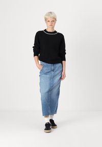 Črna pletena jopica z belim robom pri izrezu, v kombinaciji s svetloblu denim midi krilom in črnimi čevlji s bež podplatom.