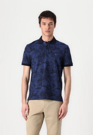 Marineblå polo shirt med et sort bladmønster, korte ærmer, og sort krave. Har et lille logo på brystet og en klassisk pasform.