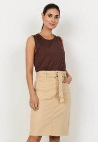 Haut sans manches marron associé à une jupe beige longueur genoux, dotée d'une taille ceinturée et de deux poches avant pour plus de fonctionnalité.