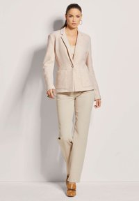 Beige blazer van textuurstof, met één knoopsluiting, twee voorzakken, gecombineerd met lichtbeige broek en bruine hakken.