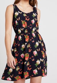 Šaty s květinovým potiskem v námořnické modři, s kulatým výstřihem, bez rukávů, s nařaseným pasem a barevnými růžemi a motýly po celém povrchu.