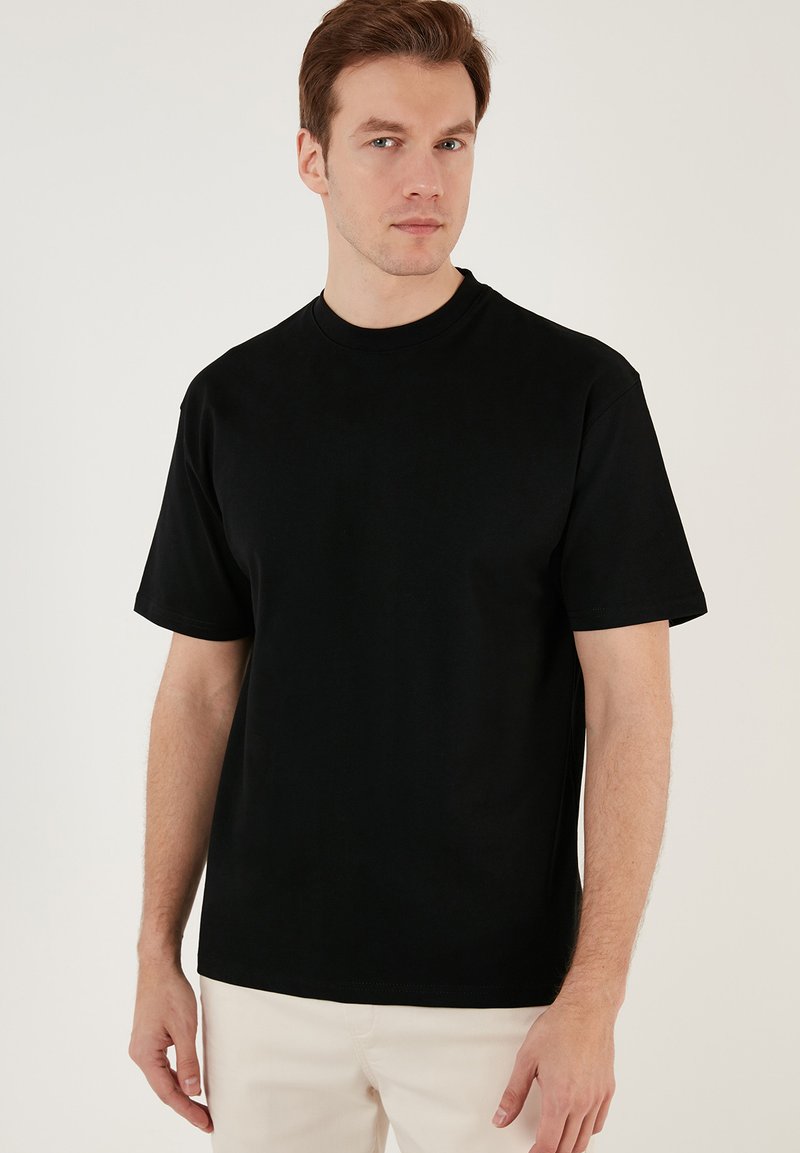 Tricou din bumbac negru cu guler rotund și mâneci scurte. Design simplu, uni, cu o croială lejeră și o textură netedă.