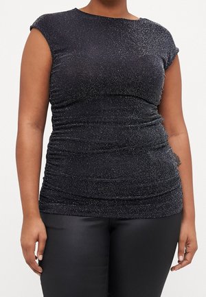 Woman wearing a fitted, short-sleeve black top with glitter details and black pants, standing against a plain background.
