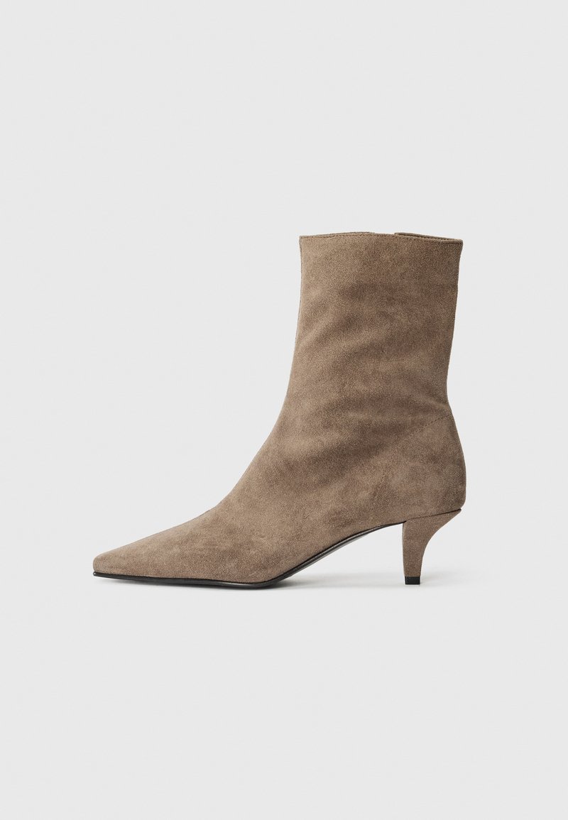 Bottine en daim marron avec un bout pointu et un talon court et fin. Texture lisse avec un design simple, sans coutures.