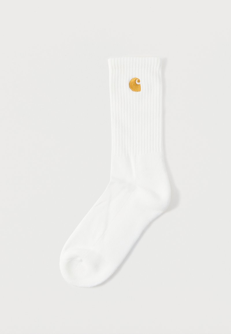 Witte katoenen sokken met geribbelde textuur, voorzien van een klein gouden logo aan de bovenzijde. Zacht materiaal; uniseks ontwerp.