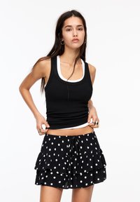 Schwarzes, geripptes Tanktop mit weißem Rand, kombiniert mit einem geschichteten schwarzen Rock mit weißen Polka-Dots. Beide Teile haben einen lockeren Schnitt.