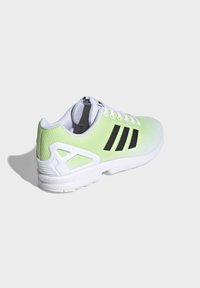 Green and white athletic shoe with a textured mesh upper, three black stripes, and a white sole featuring distinct design accents.