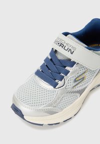 Baskets de sport argentées avec des accents bleus, tige en maille et logo proéminent. Équipées de lacets bleus et d'une semelle rembourrée pour le confort.