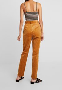 Bruna kordbyxor med rak bendesign, med hög midja och subtil horisontell ribbstruktur. Svarta sandaler fulländar looken.