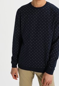 Felpa a manica lunga di colore navy, realizzata in un tessuto morbido, con piccoli motivi decorativi bianchi e azzurri. Collo rotondo e polsini a costine.