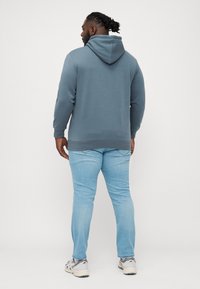 Light blue hoodie with a hood, ribbed cuffs, and hem, paired with light jeans. The fabric is smooth with a relaxed fit.