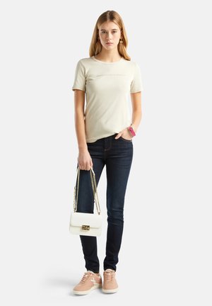 T-shirt beige clair à manches courtes, jeans bleus, baskets roses et sac à main blanc avec un fermoir doré. Design simple, look décontracté.