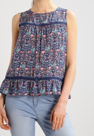 Ærmeløs navyblå bluse med farverigt blomsterprint, blonde detaljer og flæsekant, båret med lyseblå jeans.