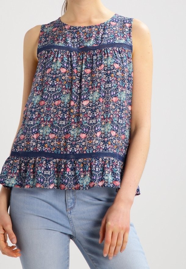 Blouse bleu marine sans manches avec motif floral coloré, détails en dentelle et ourlet à volants portée avec un jean bleu clair.