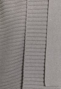 Grått stickat tyg med olika texturer: ribbade och släta sektioner, med en mjuk, matt finish och en enhetlig färgpalett.