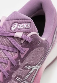 Gros plan d’une chaussure de course Asics violette avec tissu texturé, lacets et col rembourré.