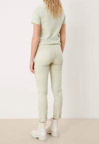 Ljusgrön åtsittande t-shirt tillsammans med ljusgröna skinny jeans och vita ankelboots. Slät tygkvalitet med en enkel design och viktiga ärmslut.