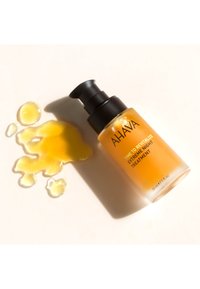 Flaske med AHAVA Time to Revitalize Extreme Night Treatment serum med pumpe ved siden af spildt gul væske på hvid overflade.
