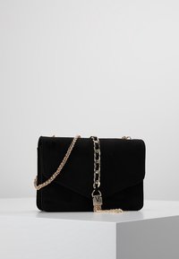 Borsa in suede nero con chiusura a patta, tracolla a catena color oro e dettaglio decorativo con lucchetto. Forma rettangolare compatta.