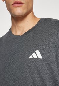 Gray, textured athletic t-shirt with a V-neck and white logo featuring three diagonal stripes positioned on the left side.