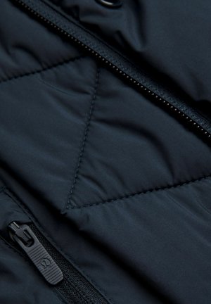 Nahaufnahme von dunklem, gestepptem Stoff mit sichtbaren Nähten und schwarzem Reißverschluss mit Marken-Zip-Anhänger an einer Jacke.