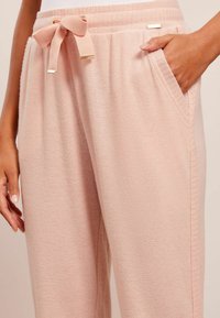 Roze gebreide broek met een gestructureerde stof, voorzien van een gestrikt tailleband en zijzakken. Het tailleband heeft een gouden accentdetail.