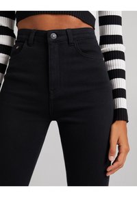 Černé džíny s vysokým pasem, hladkým povrchem, pěti kapsami a metalickým zapínáním na knoflík v pase.