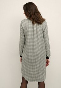 Abito a scacchi bianco e nero con maniche lunghe, orlo arrotondato e polsini neri. Tessuto leggero con vestibilità rilassata per il comfort.