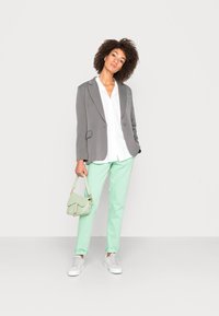 Blazer cinza, camisa branca, calças verde menta, sapatilhas brancas e uma bolsa verde-clara. Silhueta de corte reto, textura suave e design casual.