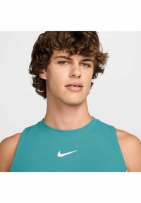Top atlético sin mangas en color verde azulado con una superficie texturizada, con el logo blanco de Nike en el pecho. Escote redondo simple y diseño ajustado.