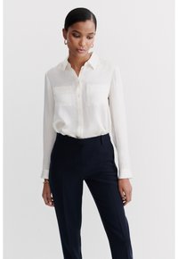 White button-up blouse with long sleeves and two chest pockets, paired with navy tailored trousers. Satin-like fabric with smooth texture.