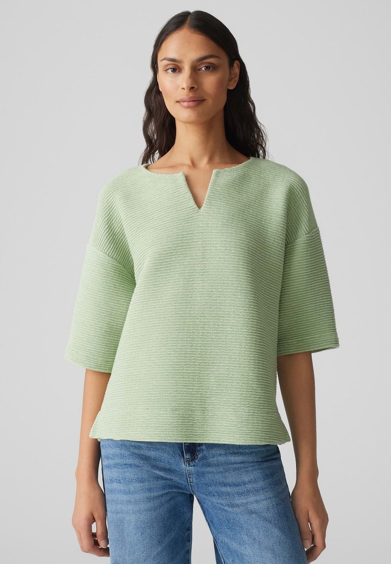 Haut vert clair texturé avec un col en V, des manches courtes et une coupe décontractée, associé à un jean en denim bleu.