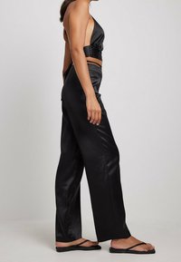 Haut court en satin noir avec un décolleté en V profond et des détails plissés, associé à un pantalon noir à jambes larges, complété par des tongs plates noires.