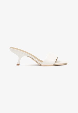 Mules blancs à bout ouvert avec une large sangle lisse et un talon fin et courbé. Le matériau semble brillant avec une semelle intérieure beige.