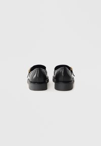 Black leather shoes with a smooth texture, rounded toe, and low black sole. Features a small gold accent near the heel.