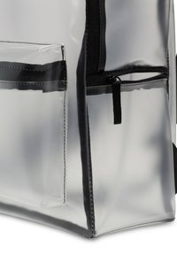 Gjennomsiktig ryggsekk med svarte detaljer, som har en teksturert, blank finish, en frontlomme med glidelås og forsterkede sømmer.