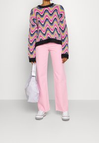 Maglione lavorato a maglia multicolore con motivo a zigzag nei colori rosa, viola, blu e nero. Abbinato a jeans a zampa d'elefante rosa chiaro e sneakers bianche.