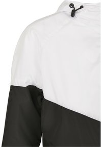 Manche et épaule de veste bicolore blanc et noir avec un cordon noir réglable à bouton au col.