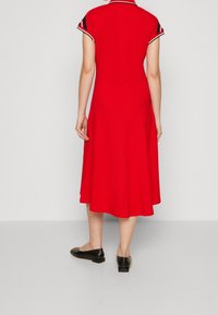 Rode jurk met korte mouwen, witte en marineblauwe accenten op de kraag en mouwen, uitlopende rok, gladde textuur, gecombineerd met zwarte ballerina's.