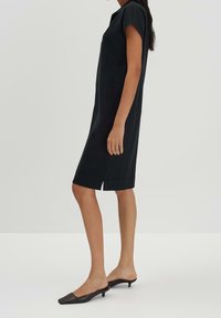 Czarna sukienka do kolan z krótkimi rękawami, luźny krój, rozcięcie po bokach i miękka faktura. W zestawie z czarnymi czółenkami na spiczastym obcasie.