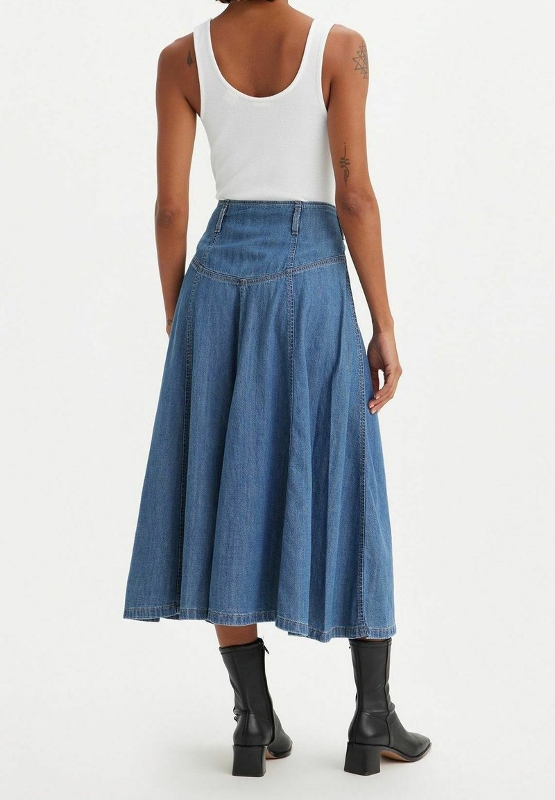 Jupe maxi en denim bleu au design évasé, taille haute et coutures subtiles. Associée à des bottines noires pour le contraste.
