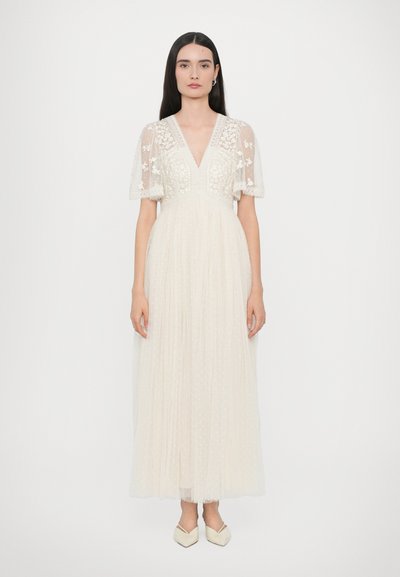 Robe longue ivoire avec des manches courtes transparentes brodées, un décolleté en V et une jupe plissée. Présente des détails floraux et un corsage ajusté.