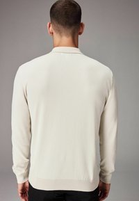 Pulóver de manga larga color beige claro, con una textura suave, puños y dobladillo acanalados. Presenta un cuello sutil y un detalle de costura mínima.