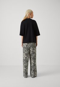 T-shirt noir oversize à manches courtes associé à un pantalon large avec un motif serpent en noir et blanc. Texture lisse, coupe décontractée.