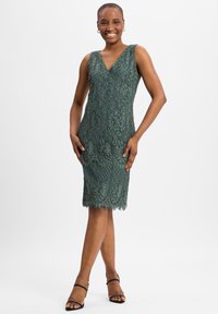 Groene kanten jurk met een V-hals, aansluitend ontwerp en gegolfde zoom. Kenmerkt zich door ingewikkelde bloemmotieven en een gladde textuur.